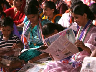 a group of women sit at a BMC election rally reading newspapers