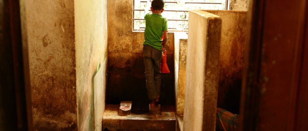 A boy washes his hands in a toilet with his back to the camera
