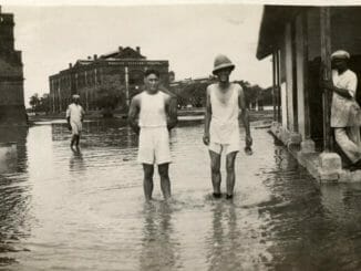 a scanned photo of floods in 1930s mumbai. two men stand in a heavy waters