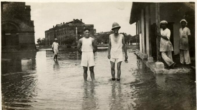 a scanned photo of floods in 1930s mumbai. two men stand in a heavy waters