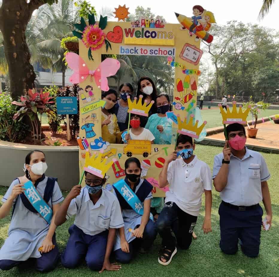 students and teachers pose for a photo in front of a photo op that says 'welcome back to school' at Jai Vakeel Foundation.