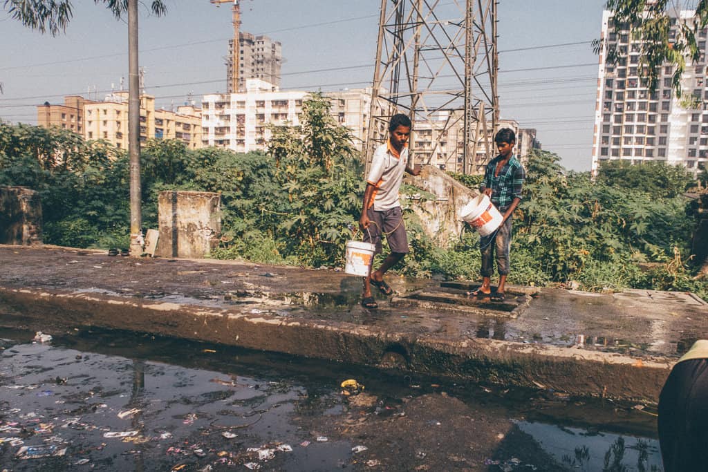 Dos hombres cargan contenedores para recolectar agua en un camino lleno de baches en Mumbai