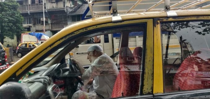 Sain Ullah Khan sits in the driver's seat of a black and yellow taxi.