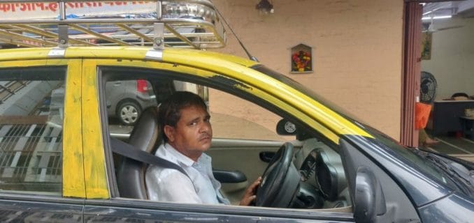 Sanjay Gupta in the driver's seat of a black and yellow cab looking at the camera.