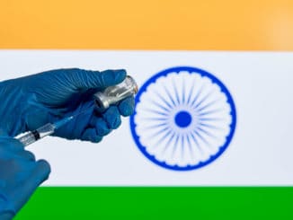 image of a medical professional's hand preparing a covid-19 vaccination, against the backdrop of the Indian flag