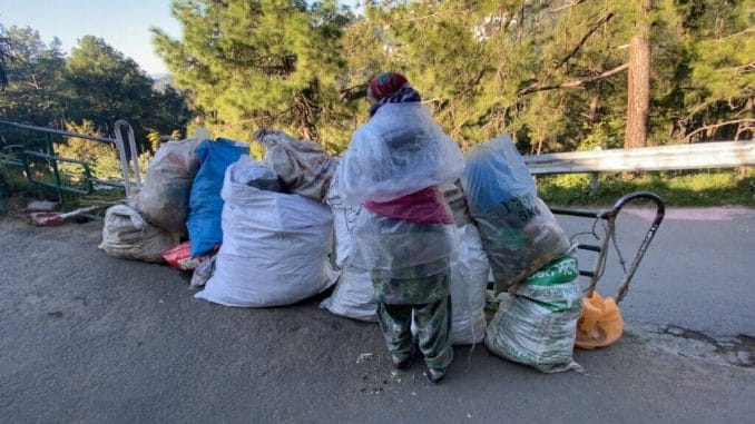 A female waste worker stands next to huge bags of garbage 